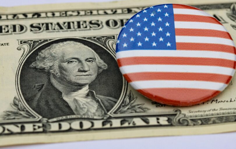 Billet de un dollar à l'effigie de George Washington, sur lequel est posé un badge rond au drapeau américain