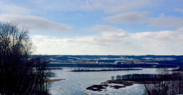 Pente enneigée au sommet de Chestnut Mountain Resort, avec en contrebas le Mississippi gelé, ses îles et les collines de l'Iowa sous un ciel nuageux
