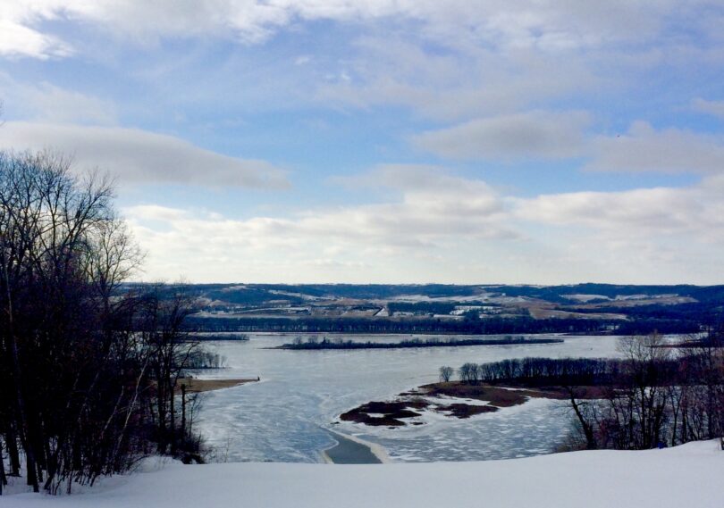 Pente enneigée au sommet de Chestnut Mountain Resort, avec en contrebas le Mississippi gelé, ses îles et les collines de l'Iowa sous un ciel nuageux