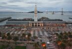Vue en hauteur du Ferry Building de San Francisco au crépuscule, tour de l'horloge illuminée, Embarcadero bordé de palmiers, baie et Bay Bridge en arrière-plan