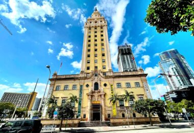 La Freedom Tower, tour ocre de style néo-espagnol du Miami Dade College, sous un ciel bleu, entre les gratte-ciel du centre de Miami