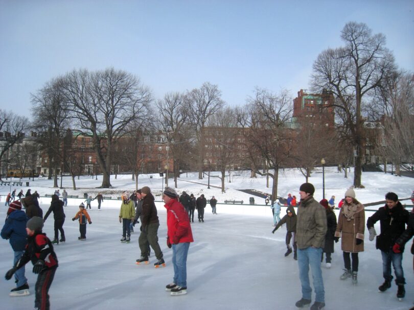 Patineurs sur la glace de Frog Pond, au Boston Common, sous un ciel bleu d'hiver, avec des arbres dénudés et de la neige autour