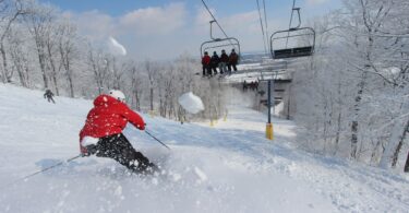 Skieur en anorak rouge sur une piste enneigée de Liberty Mountain, sous les arbres givrés, avec un télésiège en arrière-plan