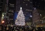 Le grand sapin illuminé du Rockefeller Center, de nuit, entre les gratte-ciel, devant une foule de visiteurs