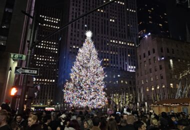 Le grand sapin illuminé du Rockefeller Center, de nuit, entre les gratte-ciel, devant une foule de visiteurs