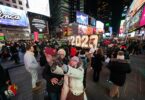 Foule de nuit à Times Square, entre les écrans géants, devant les grands chiffres lumineux « 2023 » installés pour le réveillon ; un couple se prend en photo